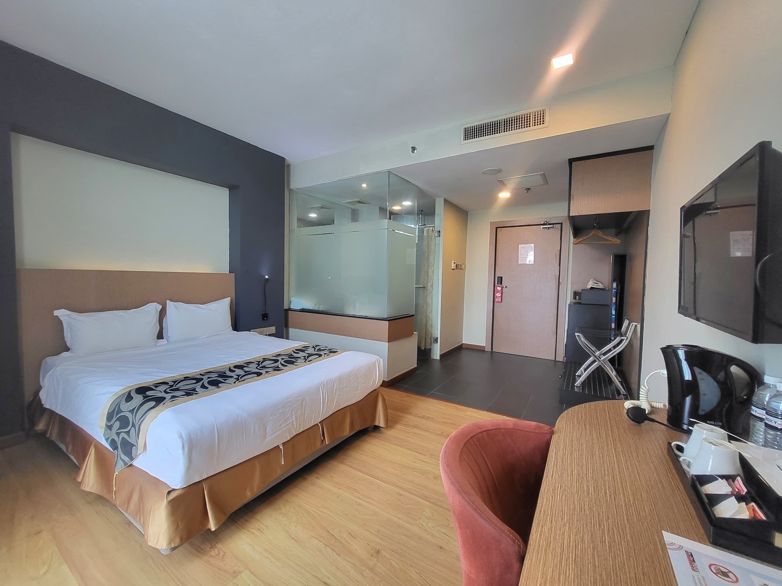 A hotel room with a bed, a desk with a chair, a coffee machine, and a TV.