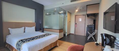 A hotel room with a bed, a desk with a chair, a coffee machine, and a TV.
