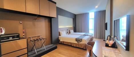 A hotel room with a wooden floor, a bed with white linens, a desk with a chair, a TV, and a minibar.