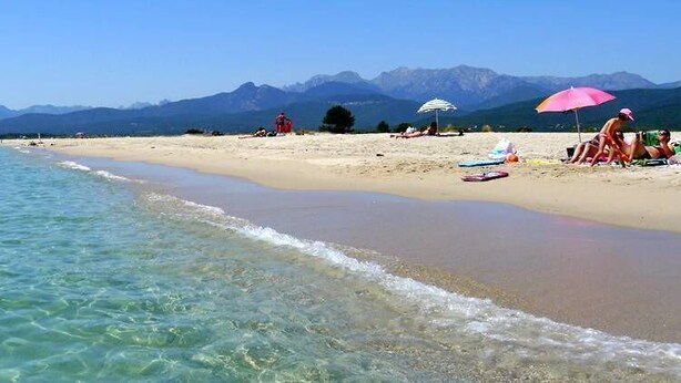 A beach with clear water, a sandy shore, and mountains in the background.