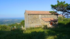 A stone building with a tiled roof, surrounded by greenery and overlooking a valley.