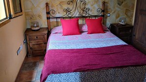 Ein Schlafzimmer mit Steinwand, Holzbettgestell, gemustertem Bettbezug und zwei roten Kissen.