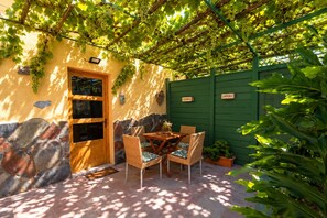 A covered patio area with a table and chairs, a stone wall, and a green fence. - San bartolome de tirajana casa rural casa rural private pool wi-fi Gratis (Santa Lucia De Tirajana)