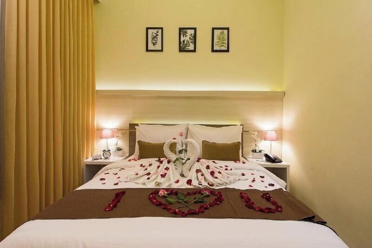 A hotel room with a bed, two bedside tables, a nightstand, a lamp, and a curtain.
