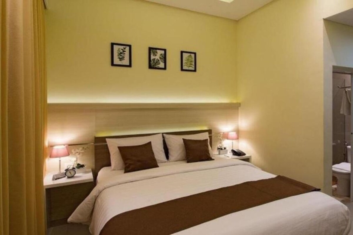 Habitación de hotel con cama, mesitas de noche y puerta de acceso a un baño.