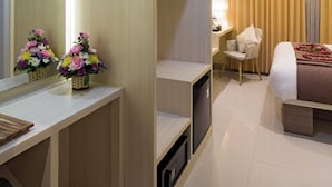 A hotel room with a bed, a desk, a chair, a mirror, and a TV. - The Xotic Jimbaran Bali (Jimbaran)