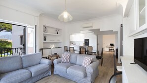 Un salon moderne avec deux canapés gris, un coin repas avec une table et des chaises, et une cuisine en arrière-plan.