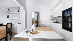 Une cuisine moderne avec des meubles blancs, un plan de travail en bois et un four noir. On y trouve également un coin repas avec une table blanche et des chaises noires.