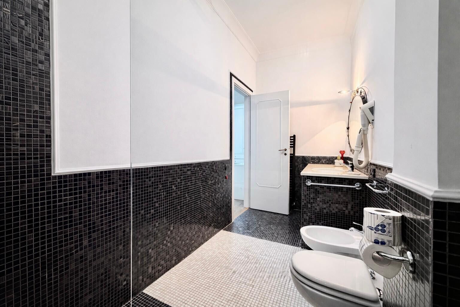Un bagno moderno con parete rivestita in piastrelle bianche e nere, un water bianco, un bidet e un lavabo con specchio.