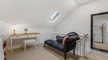 A bedroom with a sloped ceiling, a desk, a bench, a dark sofa, a large mirror, and a small window.