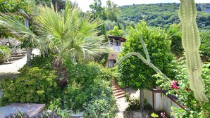 A lush garden with a variety of plants, a stone pathway, and a building with a red roof in the background. - AMORE RENTALS - Villa Bacco with Private Swimming Pool, Sea View, Parking, Romantic (Termini)