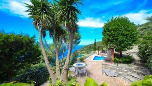 A pool area with a view of the sea, surrounded by trees and a stone wall. - AMORE RENTALS - Villa Bacco with Private Swimming Pool, Sea View, Parking, Romantic (Termini)