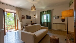Ein Wohnzimmer mit Sofa, einer Hängelampe, einer Stehlampe, einer Heizung und Blick durch ein Fenster.
