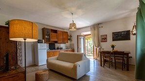 Ein gemütliches Wohnzimmer mit einer Couch, einem Esstisch mit Stühlen, einer Küchenzeile mit Holzschränken und einem großen Fenster mit Vorhängen.