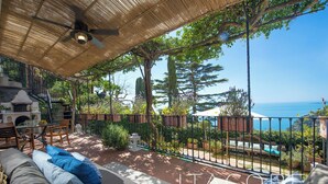A covered outdoor seating area with a view of the sea, a fireplace, and a staircase leading to an upper level. - Villa Gaia Positano - Sea View, Pool, Terrace, Patio & Courtyard (Positano)
