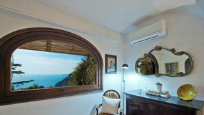 A room with a large arched window offering a view of the sea, a chair, a desk with a lamp, and a mirror on the wall. - Villa Gaia Positano - Sea View, Pool, Terrace, Patio & Courtyard (Positano)