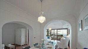 A dining area with a glass table set for four, white chairs, and a chandelier. - Villa Gaia Positano - Sea View, Pool, Terrace, Patio & Courtyard (Positano)