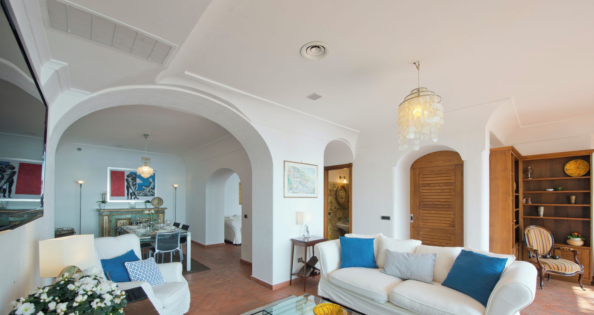 Ampla sala de estar com um sofá branco, área de refeições e cozinha visível através de um arco.
