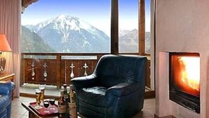 A cozy room with a leather chair, a fireplace, and a large window offering a mountain view.