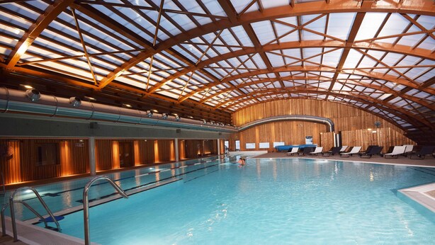 An indoor swimming pool with a high arched wooden ceiling and a view of the pool area.