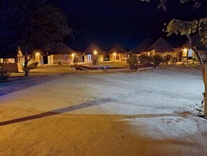 A nighttime view of a resort with thatched-roof huts, a sandy courtyard, and ambient lighting. - Kutir Village Resort (Bhuj)