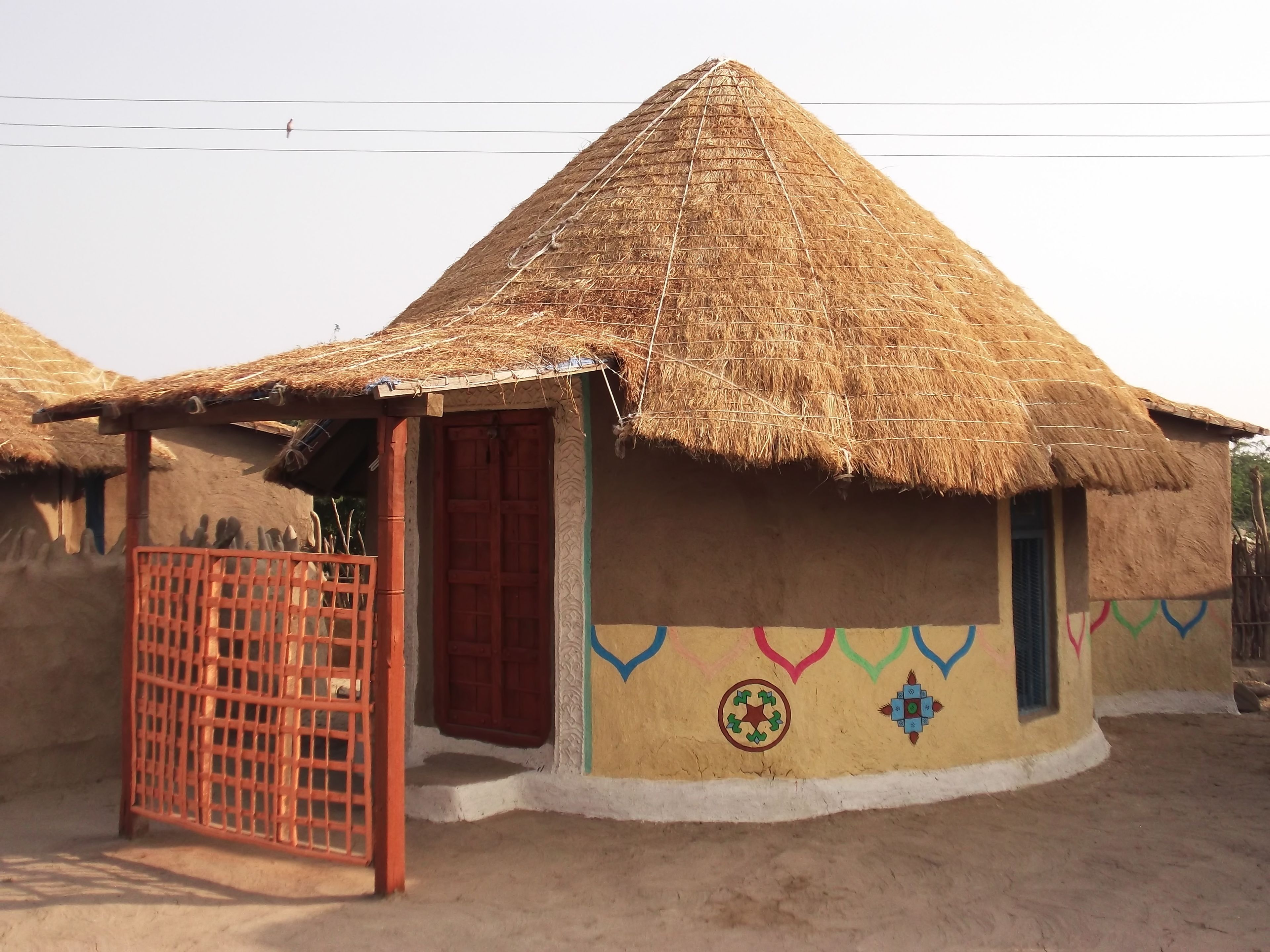 A traditional thatched-roof hut with a wooden door and a colorful painted wall.