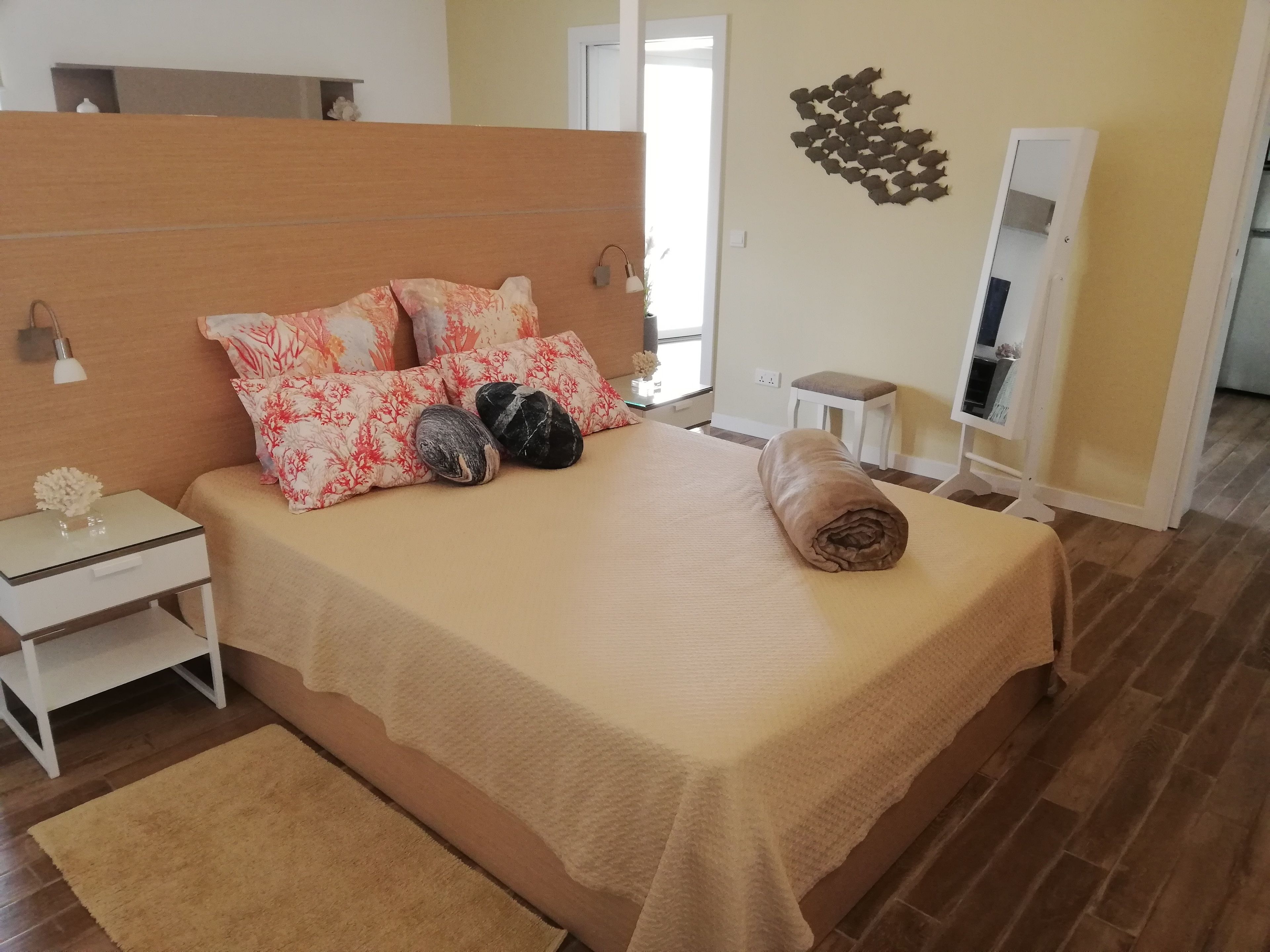 A neatly made bed with floral pillows, a bedside table with a lamp, and a small stool.