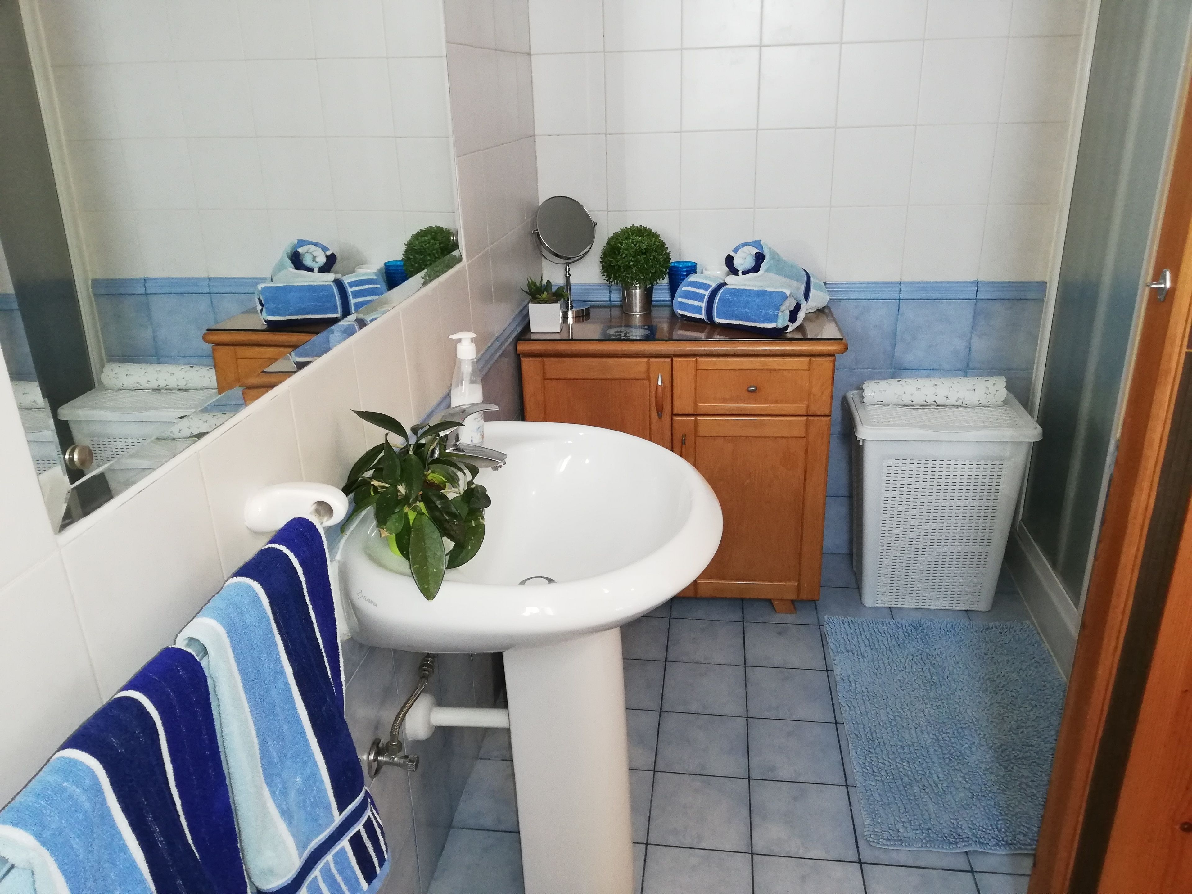 Ein Badezimmer mit einem weißen Waschbecken, einem Spiegel, einem Holzschrank und einem blauen Handtuch.
