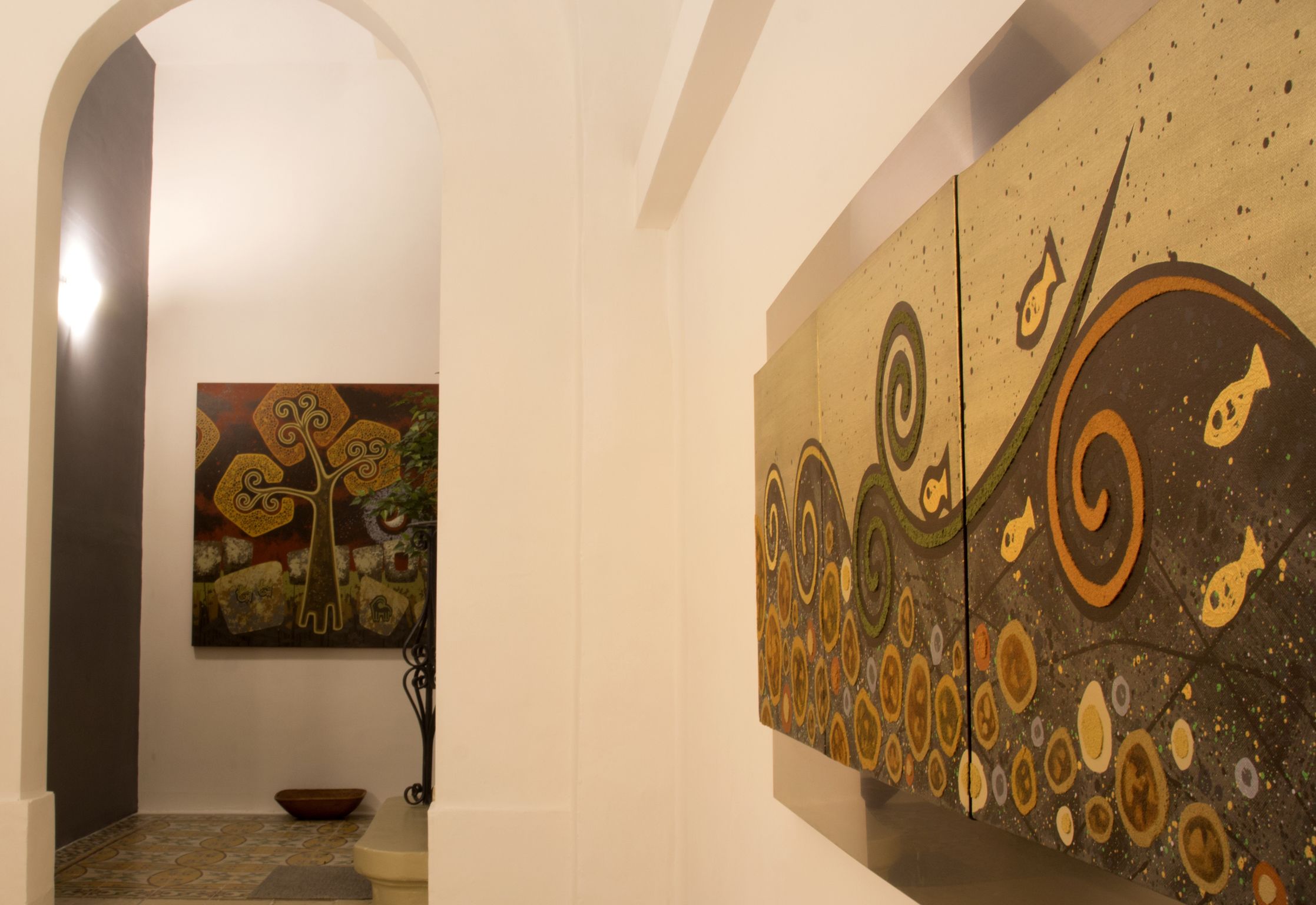 A hallway with a large abstract painting on the right wall and a smaller one on the left. There is a bowl on the floor and a staircase leading to another level.