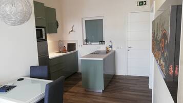Una cucina compatta con forno a microonde, lavello e una piccola isola. C'è una zona pranzo con tavolo e sedie, e una porta con segnale di uscita verde.