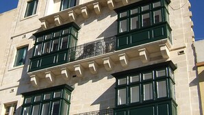 Un edificio de varios pisos con un estilo arquitectónico clásico, que presenta grandes ventanales y balcones con marco verde.