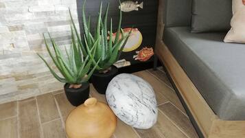Una esquina de una habitación con una planta de aloe vera en maceta, un cuenco de madera y una escultura de mármol en el suelo.
