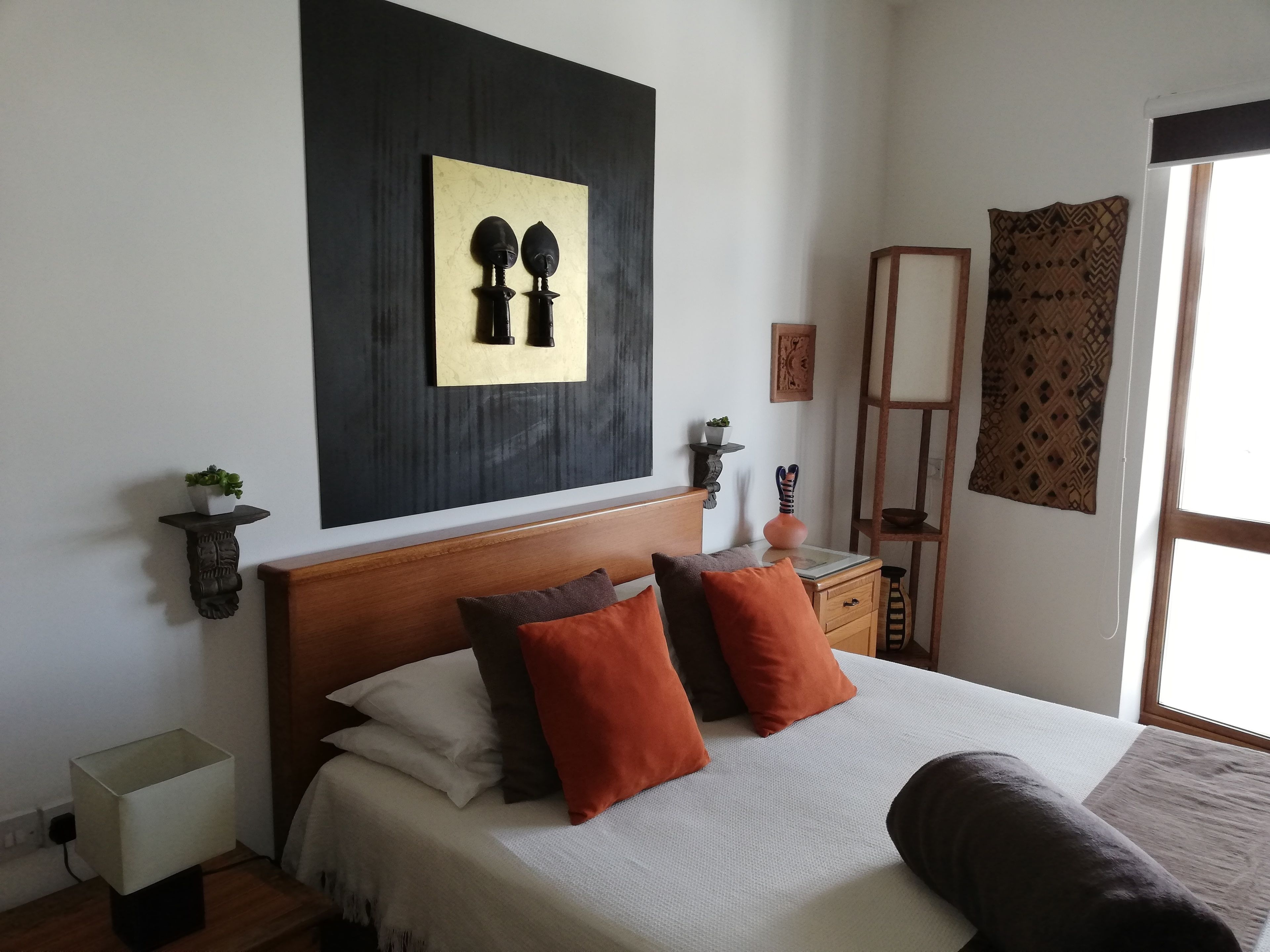 Un lit bien fait, avec une tête de lit en bois, une table de chevet avec une lampe et une œuvre d’art accrochée au mur.