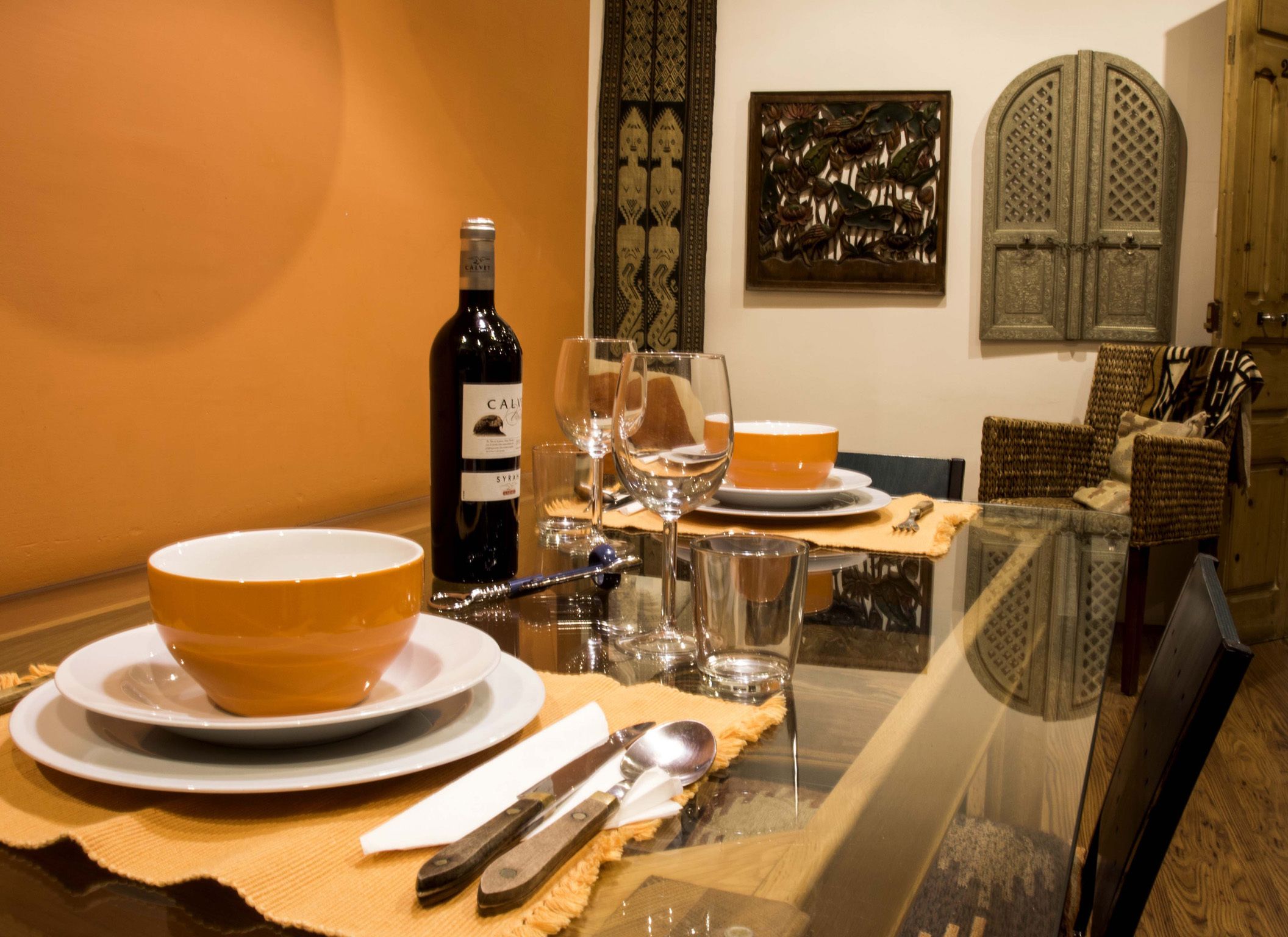 Een eettafel gedekt met borden, kommen, bestek en een wijnfles.