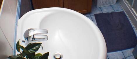A bathroom with a white sink, wooden cabinets, a mirror, a small plant, and a trash bin.