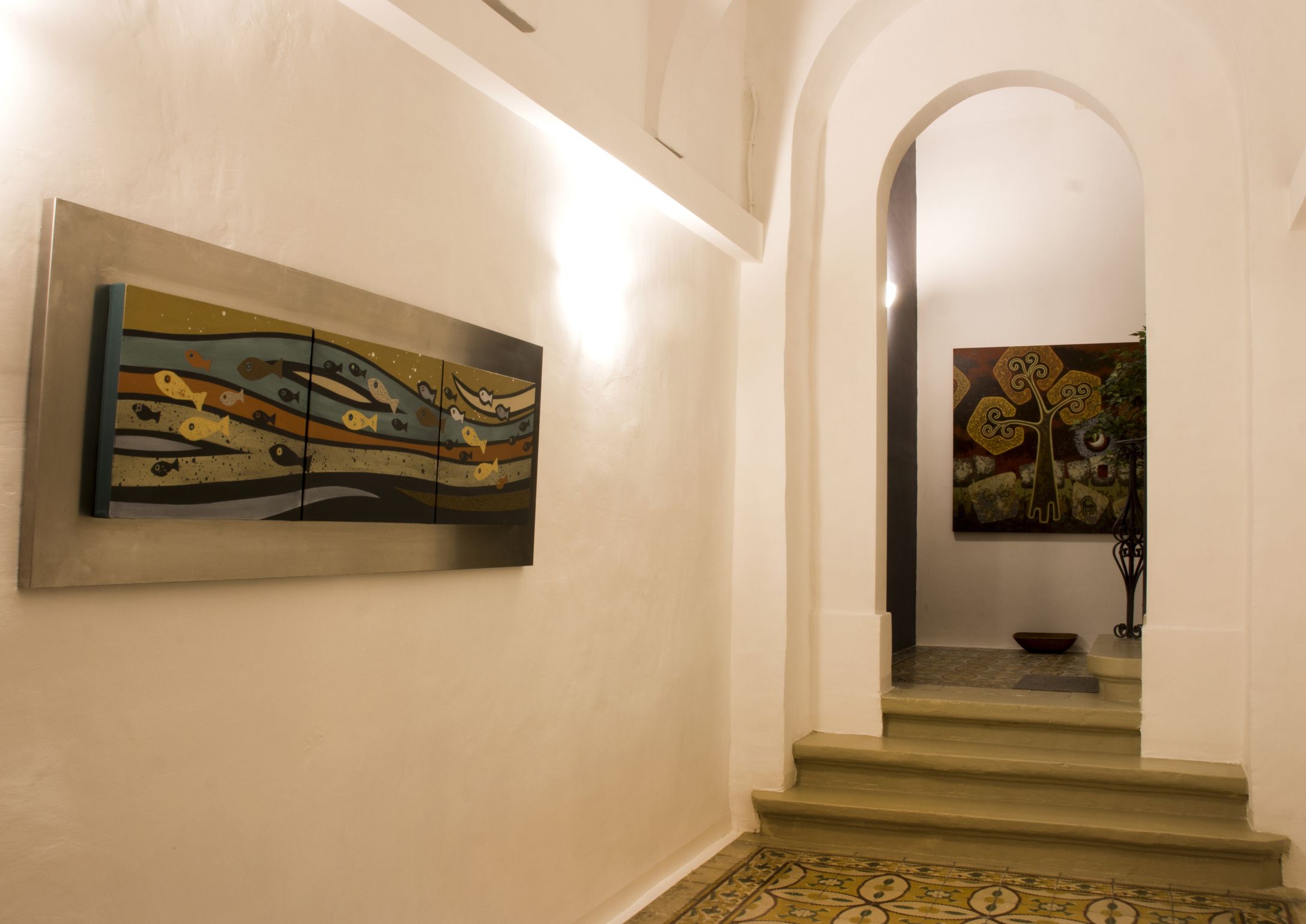 A hallway with a staircase leading to a landing. There are two artworks on the walls, one on the left and one on the right.