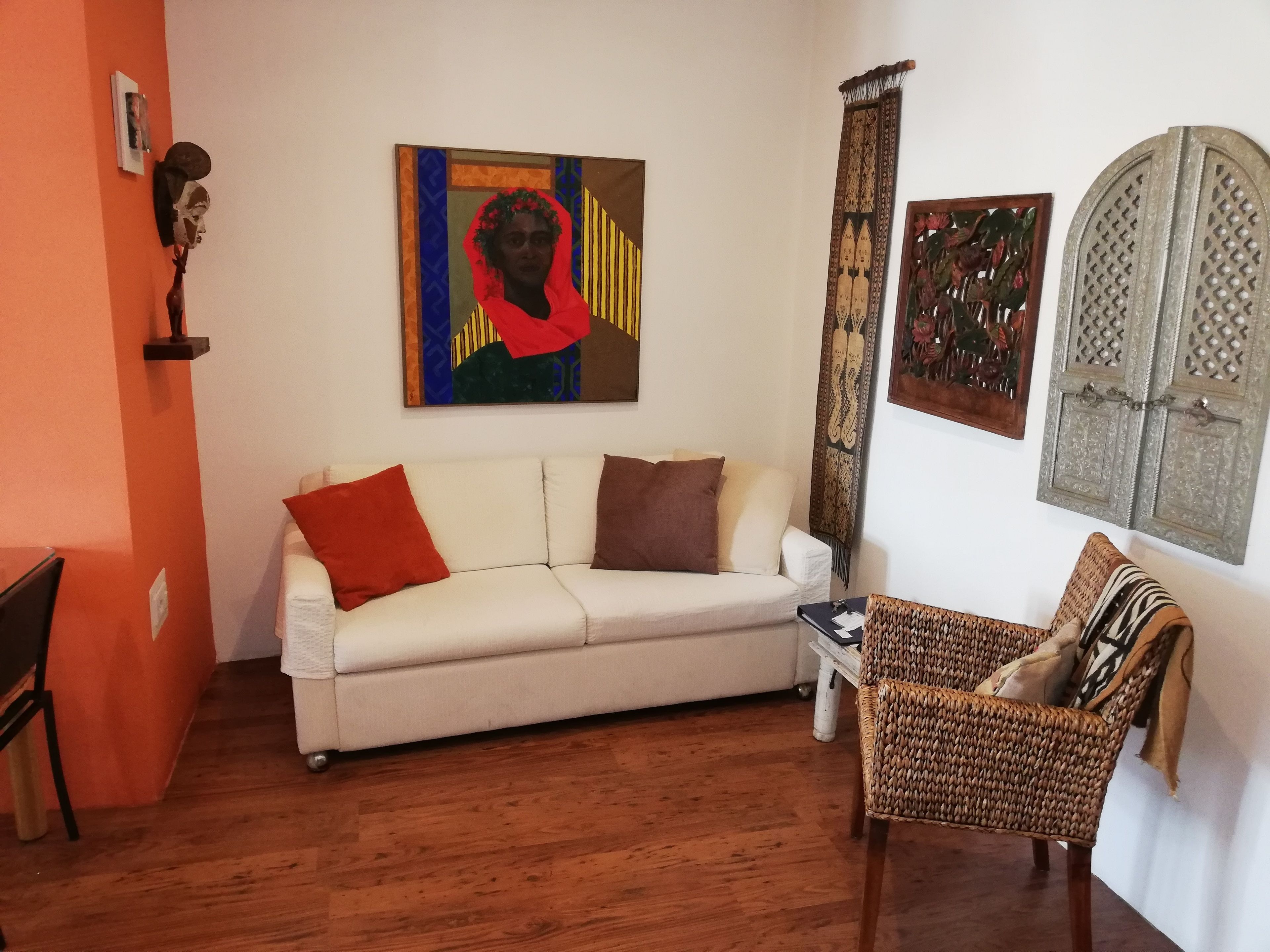 Una sala de estar con un sofá blanco, un sillón de mimbre y piso de madera.