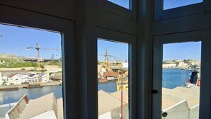 Vista desde el interior de un edificio hacia un puerto con grúas y edificios industriales.