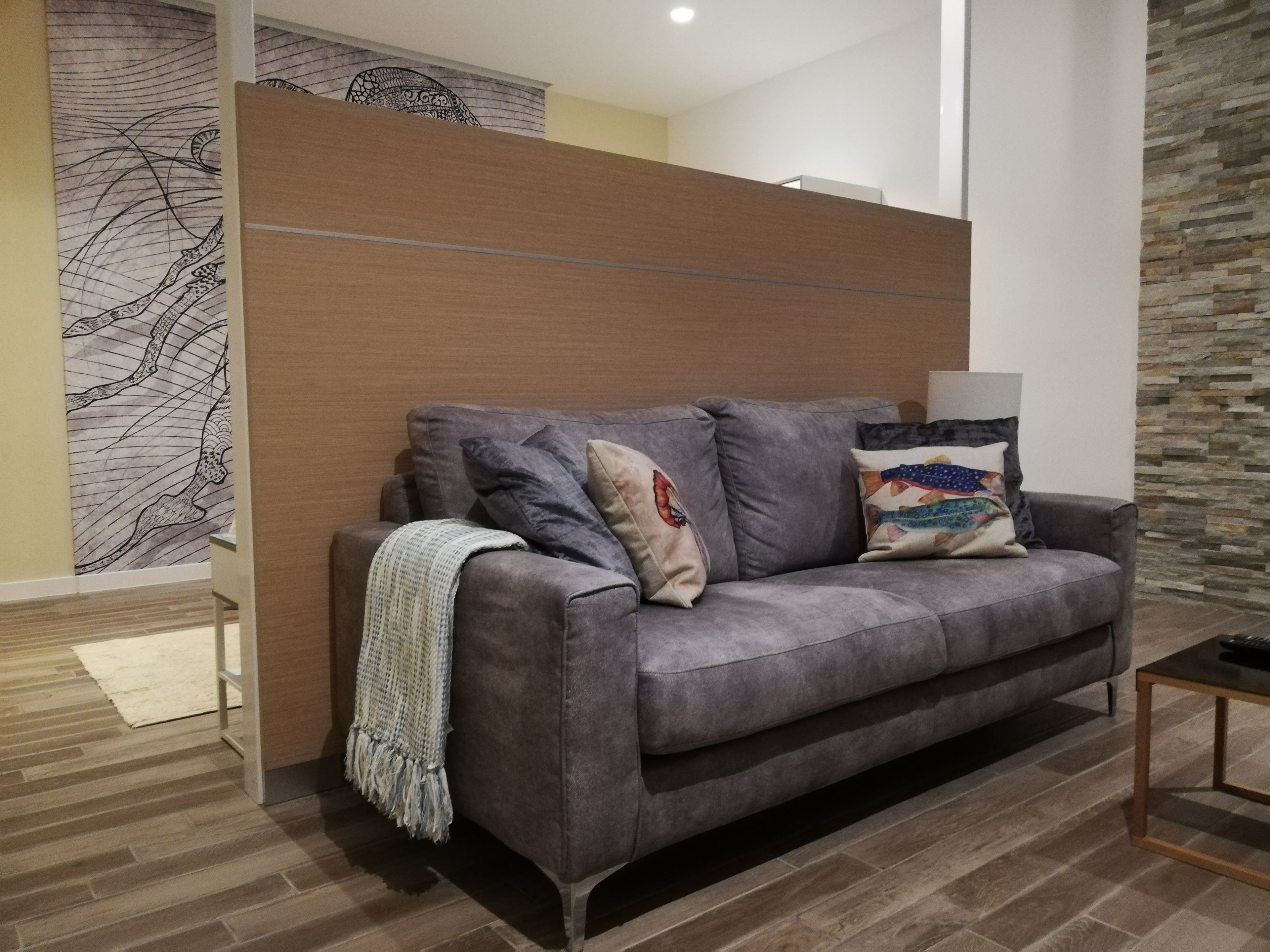 A modern living room with a grey sofa, a patterned wall, and a stone accent wall.