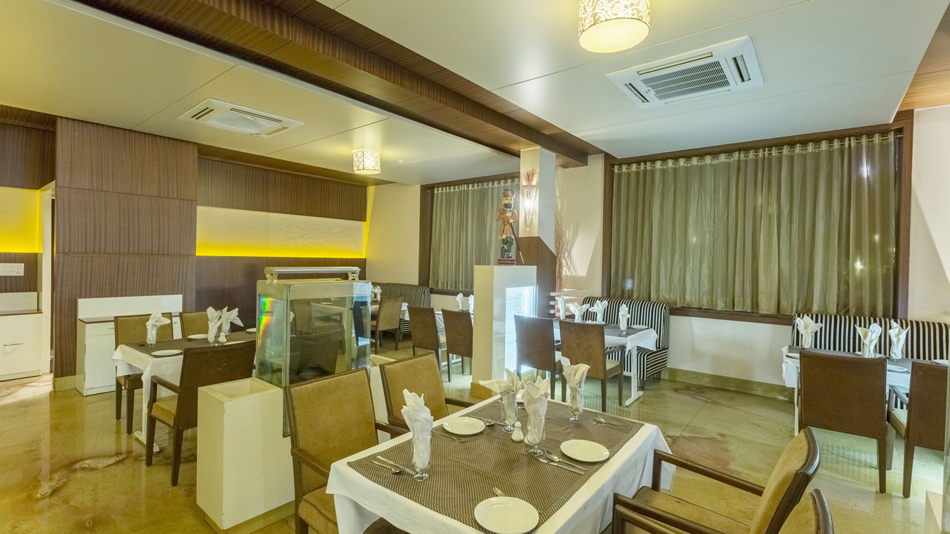 A hotel dining area with multiple tables and chairs, a reception desk, and a decorative statue.