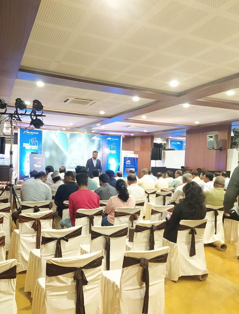 A conference room with rows of chairs, a stage with a speaker, and a large screen displaying text.