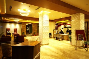 A hotel lobby with a reception desk, seating area, and decorative pillars. - Sai International Hotel (Davanagere)