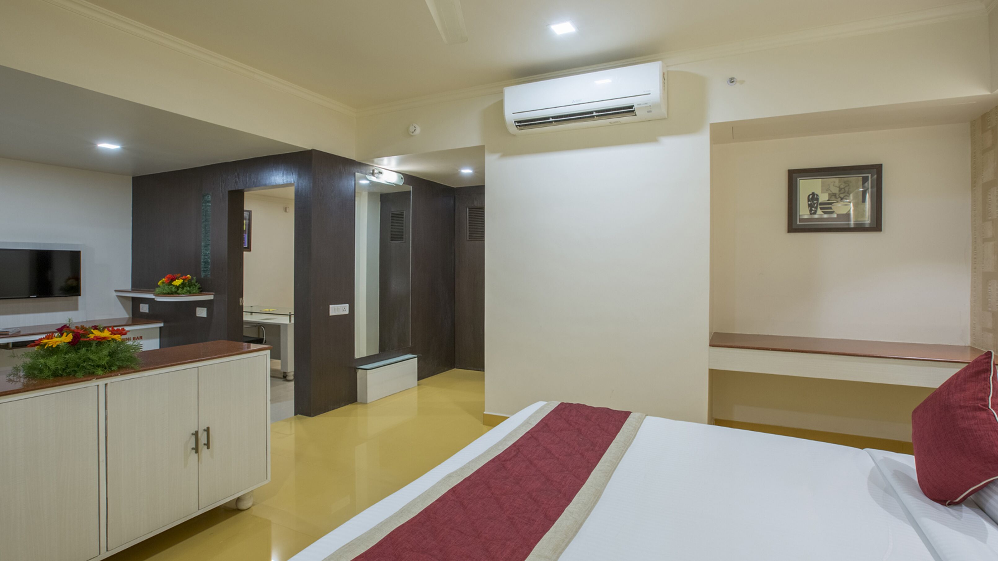 A hotel room with a bed, a desk, a mirror, an air conditioning unit, and a television.
