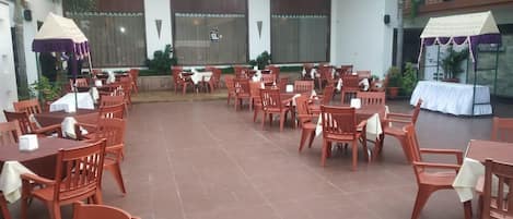 An outdoor patio with multiple wooden tables and chairs, some covered by umbrellas.