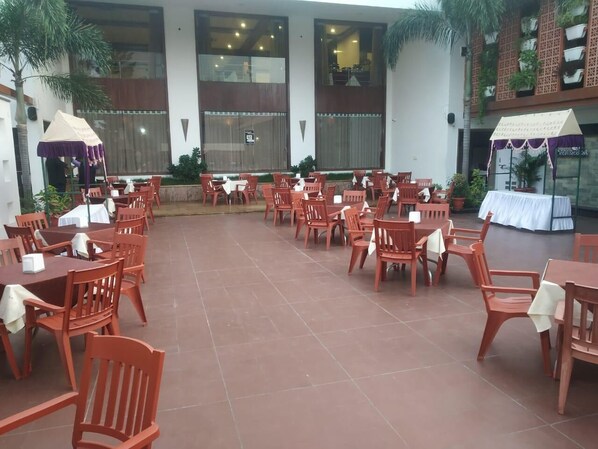 An outdoor patio with multiple wooden tables and chairs, some covered by umbrellas. - Sai International Hotel (Davanagere)