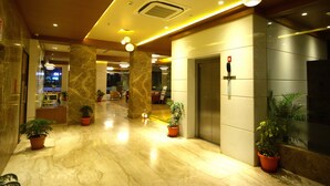Et hotel lobby med marmorgulv, krukker med planter, en receptionsdisk og en elevator.