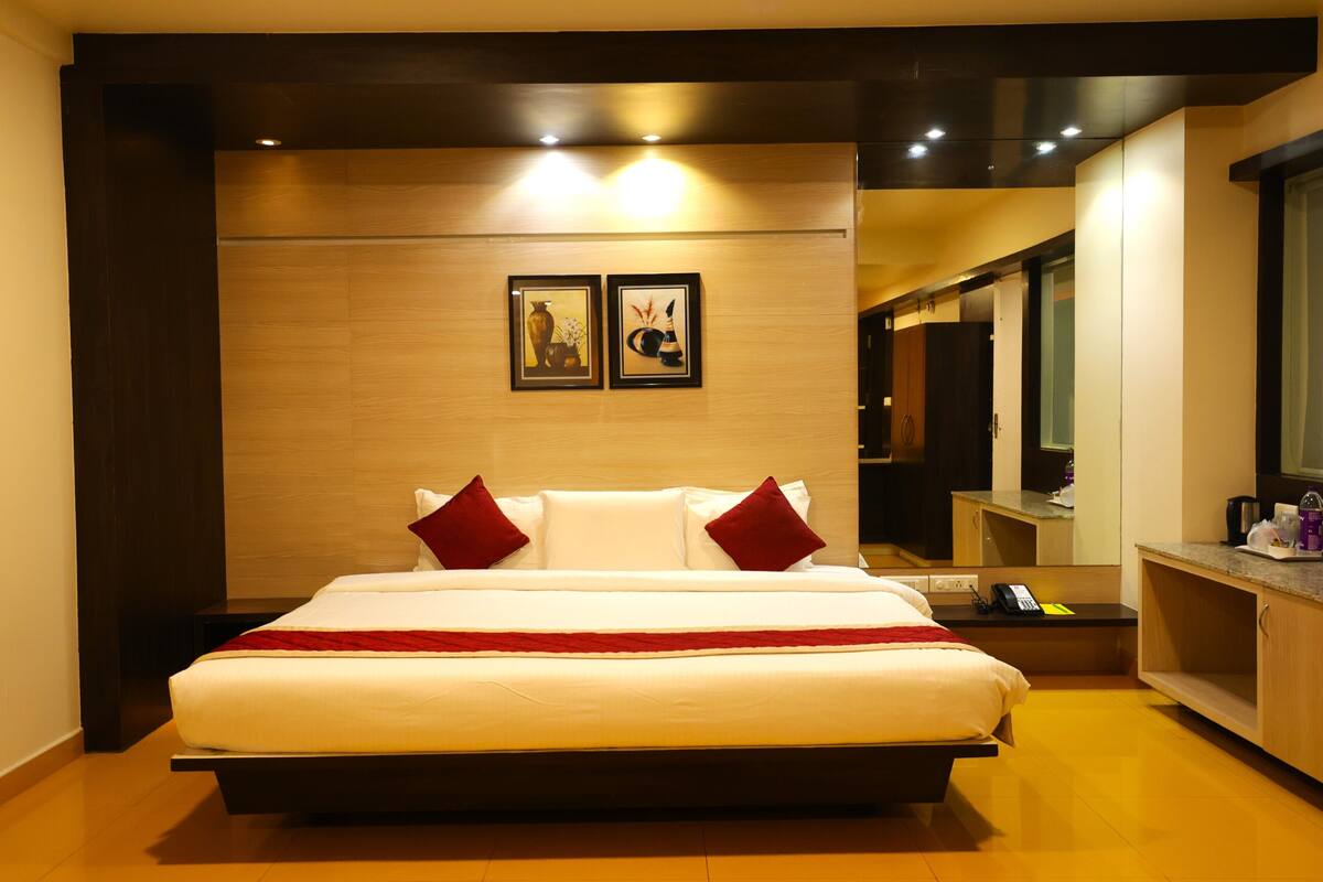Une chambre d’hôtel moderne avec un grand lit, une tête de lit en bois, une table de chevet avec un téléphone et un miroir au-dessus de la table.