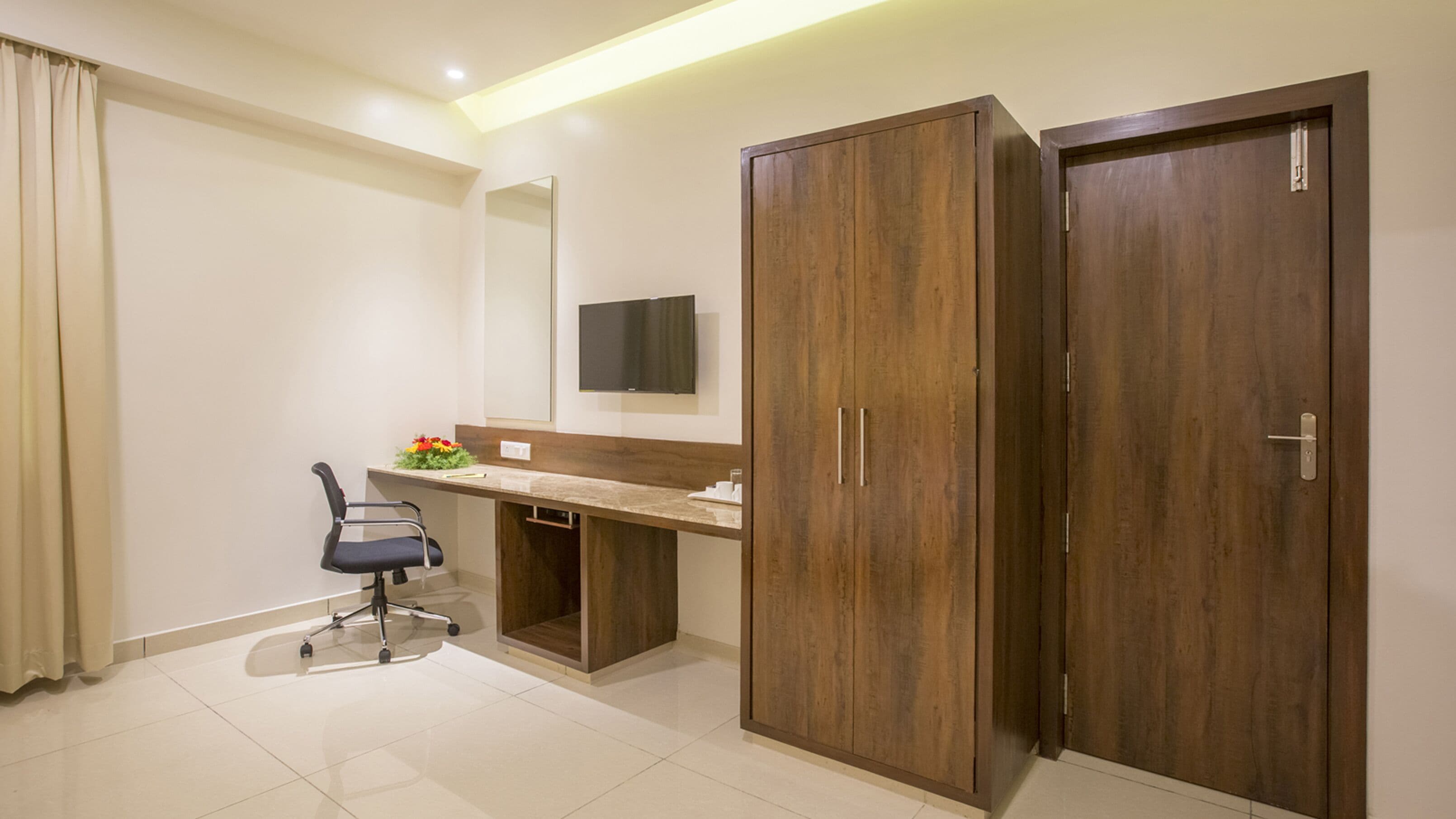 A modern office space with a desk, chair, wardrobe, and a mounted TV.