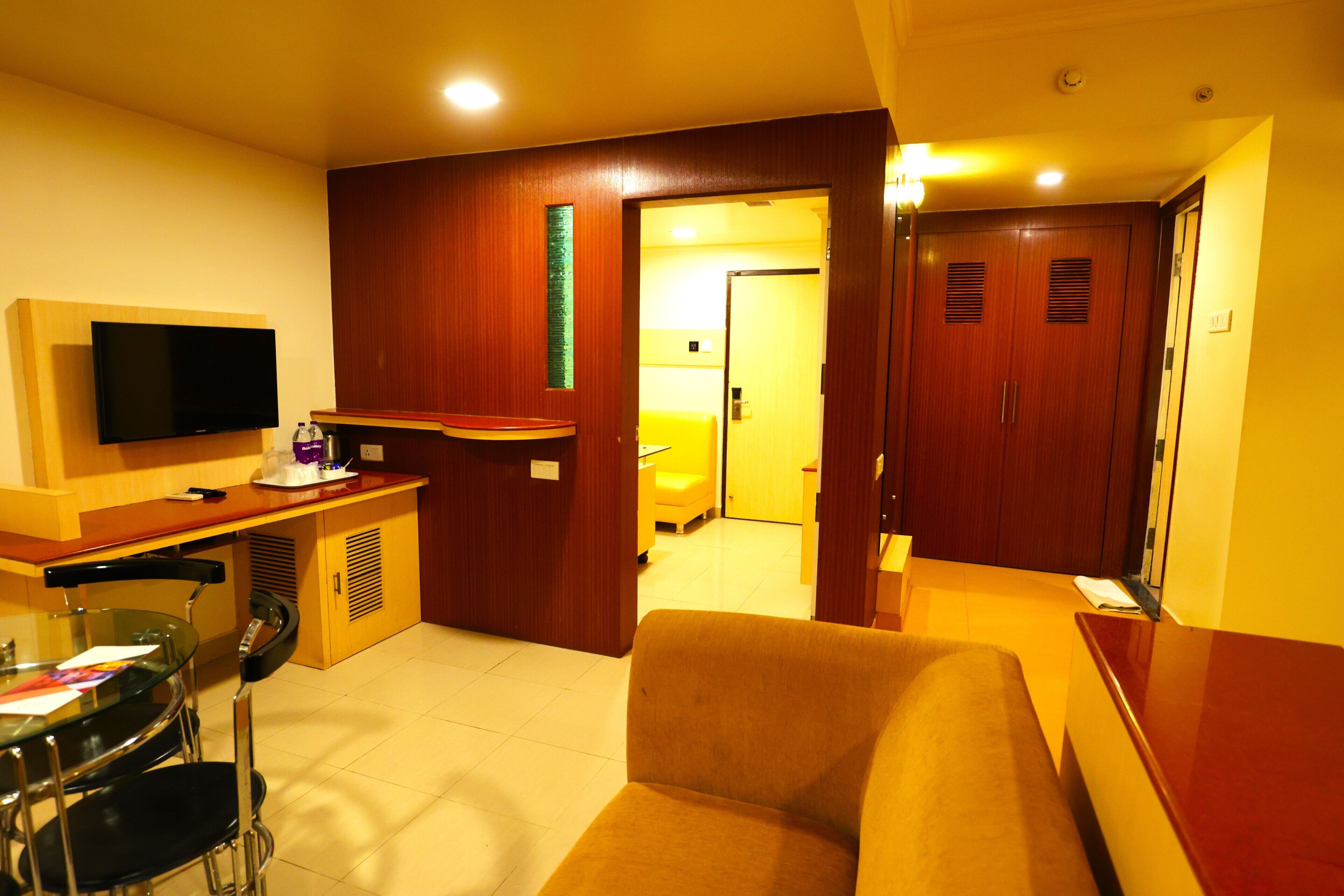 Ein Hotelzimmer mit Fernseher, einer Couch, einem Esstisch mit Stühlen und einem Holzschrank.