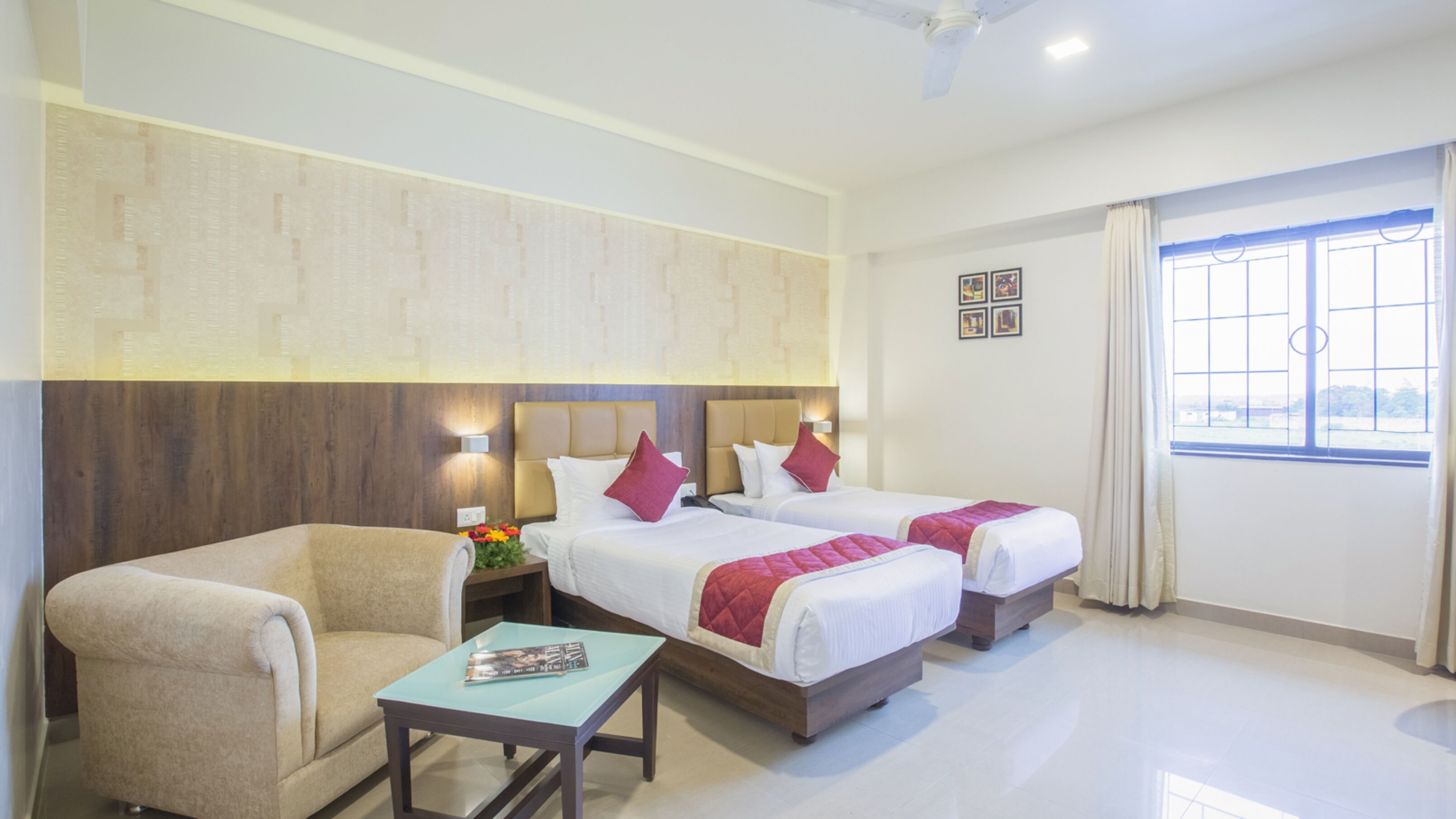 A hotel room with two beds, a chair, a small table, and a window with curtains.